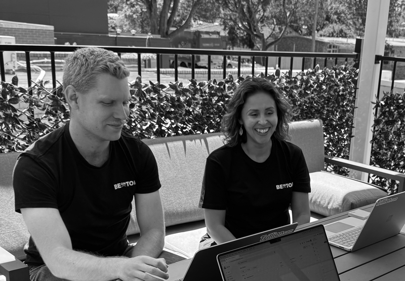 a man and woman sitting on a bench with laptops